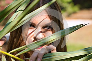 Portrait of beautiful young woman, blonde, blue eyes, looking through the leaves of a green palm tree. Beauty concept, plants,