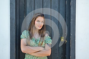 Portrait of beautiful young woman, blonde, blue eyes, wearing a green suit with flowers, smiling, leaning on the frame of a wooden