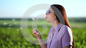 Portrait of a beautiful young woman blowing on big dandelion in the sunny day.