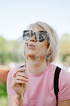 Portrait of a beautiful young woman blowing dandelion flower