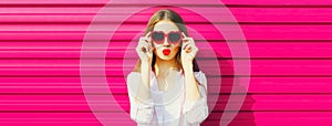 Portrait of beautiful young woman blowing her lips sending sweet air kiss with lipstick wearing red heart shaped sunglasses on