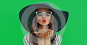 Portrait beautiful young woman blowing her red lips sending sweet air kiss wearing a summer straw hat on green