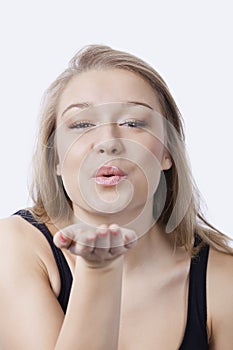 Portrait of beautiful young woman blowing kiss against white background