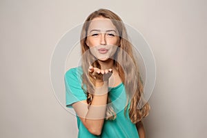 Portrait of beautiful young woman blowing kiss on light background