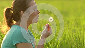 Portrait of a beautiful young woman blowing on the ripened dandelion.