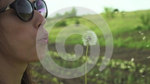 Portrait of a beautiful young woman blowing on ripened dandelion. Slow motion