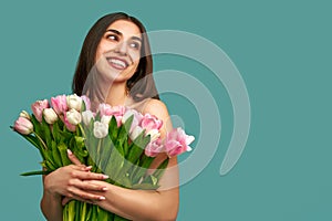 Portrait of a beautiful young woman on a blue background holding a bouquet of white and pink tulips. Spring and beauty concept