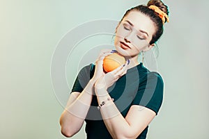 Portrait of a beautiful young woman with bun hairstyle and elegantly sandwiched orange fruit between hands,fashion portrait on