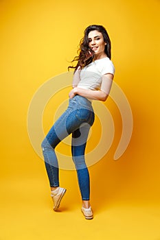 Portrait of a beautiful young woman in casual smiling and looking over her shoulder while posing on yellow studio