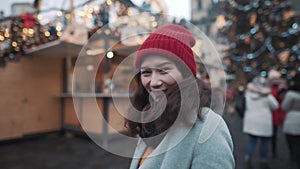 Portrait of beautiful young woman in a center of christmas fair. Girl smiling in front of christmas tree, enjoying