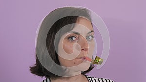 Portrait of a beautiful young woman cheerfully blowing a party horn on a purple background slow motion