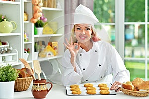 Portrait of beautiful young woman in chefs hat baking at home. OK gesture