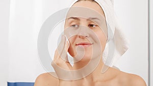 Portrait of beautiful young woman cleaning face and washing off makeup in the bathroom with cotton pad and lotion. Concept of