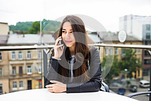 Portrait of beautiful young woman in coffee shop terrace, relaxing using smart phone, phone call conversation outdoors. Fashion fe