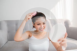 Portrait of beautiful young woman combing her hair, looking mirror