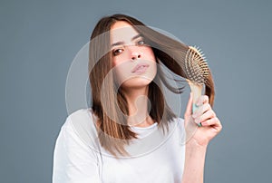 Portrait of beautiful young woman combing her hair, smiling. Female brushing healthy hair with comb. Cares about a