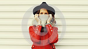 Portrait beautiful young woman covering her face with scarf wearing a red jacket, black round hat on white background