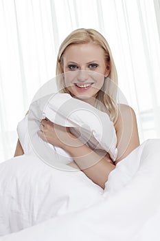 Portrait of beautiful young woman covering herself with bedsheet in bed