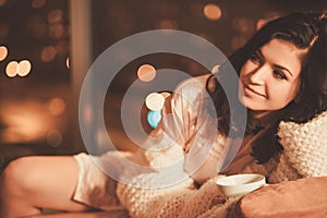 Portrait of beautiful young woman with cup of hot drink in cozy home interior