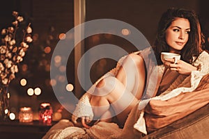 Portrait of beautiful young woman with cup of hot drink in cozy home interior