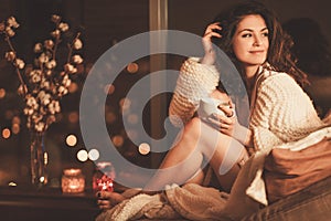 Portrait of beautiful young woman with cup of hot drink in cozy home interior