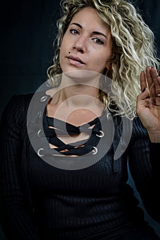 Portrait of a beautiful young woman with curly blonde hair who holds a lock of hair and looks intently