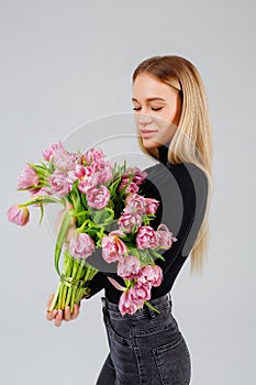 Portrait of a beautiful young woman in dark with pink tulips on a gray background, floristics