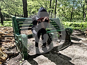 Portrait of a beautiful young woman with a depressed expression, sitting on wooden bench in local public park. Violence victim