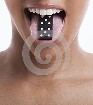 Portrait of beautiful young woman with domino on tongue against white background