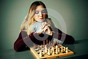 Portrait of a beautiful young woman in a dress with a frill, who is sitting in front of a chessboard and thinking about the next
