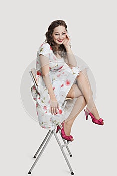 Portrait of beautiful young woman in dress sitting on stool against white background