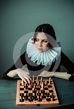 Portrait of a beautiful young woman in a dress with a white frill, who is playing chess. A difficult game. A game of chess