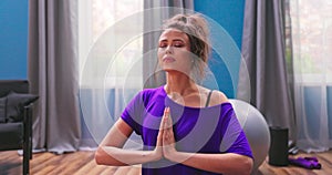 Portrait of beautiful young woman dressed in fitness clothes meditates while sitting in lotus position