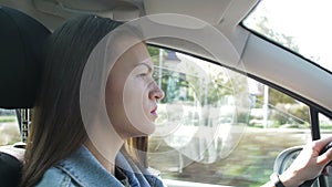 Portrait of beautiful Young Woman Driving Car through big Sunny City. Camera Shot Made From the Passenger.