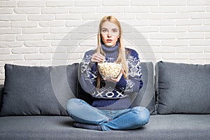 Portrait of beautiful young woman eating popcorn while watching movie in living room