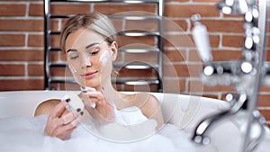 Portrait of beautiful young woman enjoying applying face cream taking bath medium close-up