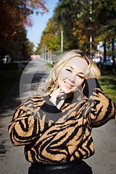 Portrait of a beautiful young woman enjoying autumn in the park. Attractive blonde in autumn park on a background of