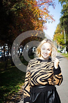 Portrait of a beautiful young woman enjoying autumn in the park. Attractive blonde in autumn park on a background of