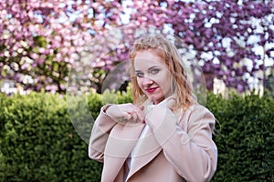 Portrait of beautiful young woman of European appearance. Strong modern woman in coat in park. Successful business woman