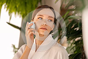 Portrait of beautiful young woman with flawless skin using silicone face brush, standing in bathroom decorated with