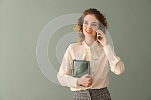 Portrait of beautiful young woman in formal clothes talking by phone on color background