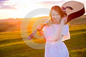 Portrait of the beautiful young woman with guitar in field