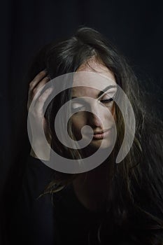 Portrait of a beautiful young woman with a hand on her head in her hair as she looks down thoughtfully