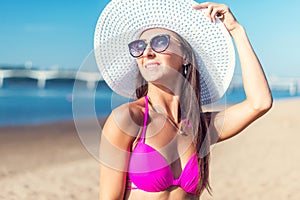 Portrait of beautiful young woman in hat posing in bikini on the beach