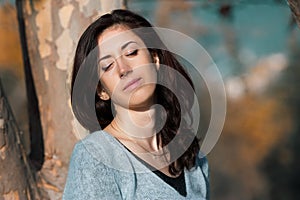 Portrait of a beautiful young woman with her eyes closed against a tree and autumn yellow foliage