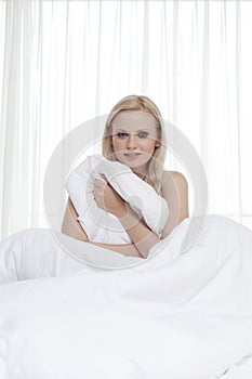 Portrait of beautiful young woman holding bedsheet in bed