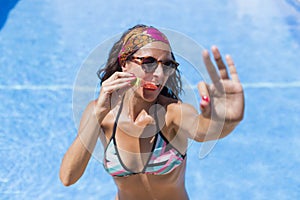 Portrait of a beautiful young woman holding a piece of watermelon and smiling. Blue Swimming pool water background. Summer and