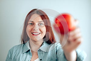 Portrait of a cheerful young woman eating red apple on gray wall background. Healthy nutrition diet. Apple vitamin snack