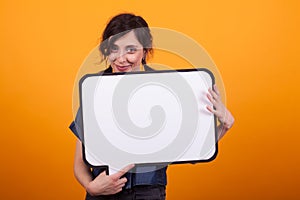 Portrait of beautiful young woman holding a white thoughts bubble in studio over yellow background