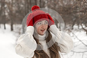 Portrait of beautiful young woman in knitted red hat and mittens and woolen sweater in winter park. Ladies knitwear